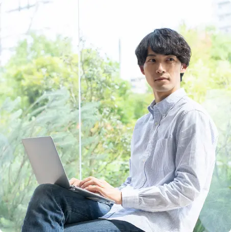 ノートパソコンを膝において作業する男性の画像