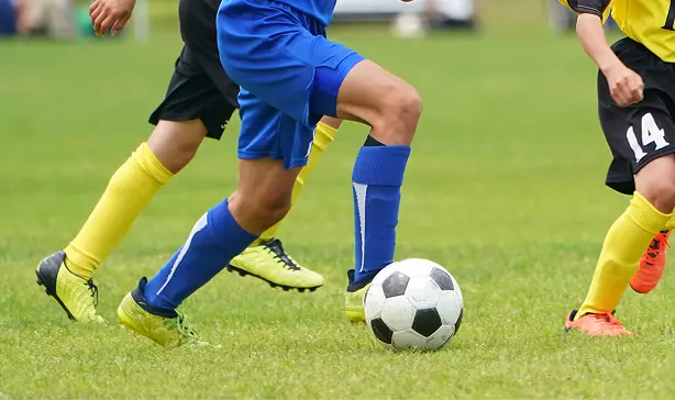 緑の芝生の上で、サッカーボールをドリブルする選手の足元のアップ